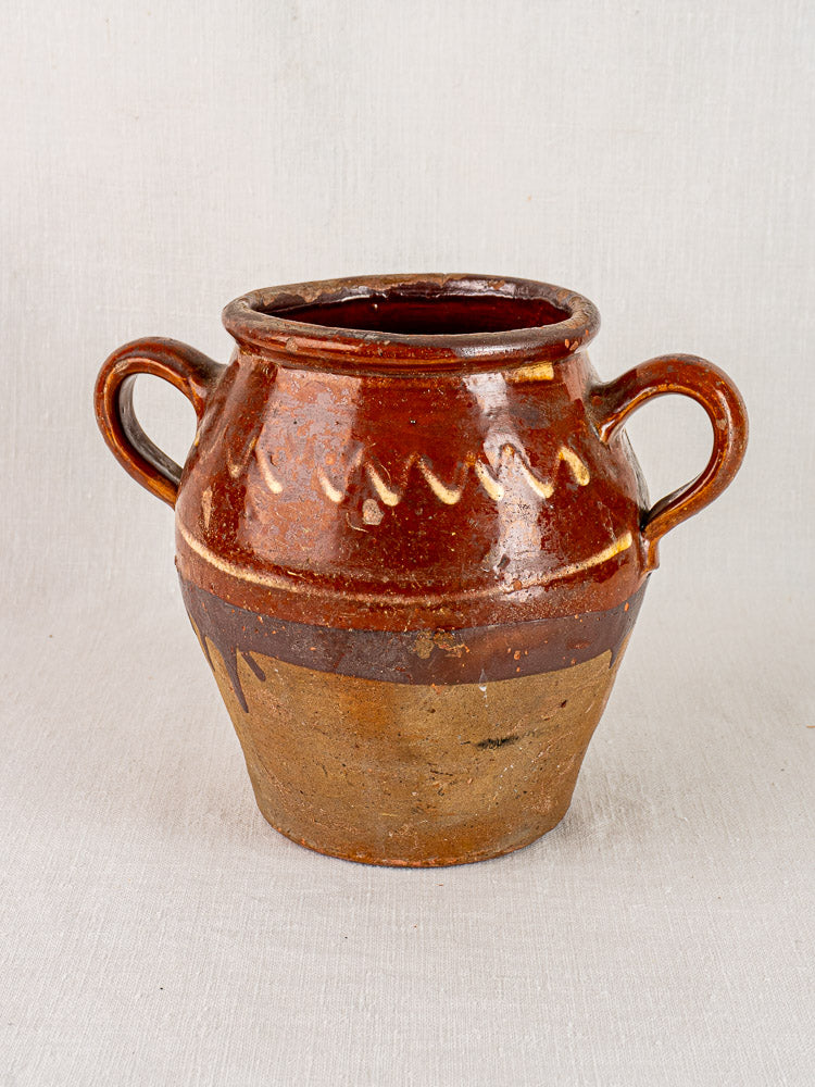 Antique French confit pot with brown glaze, yellow slipwork rim, twin handles, and matte unglazed lower section.