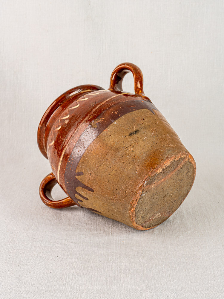 Mid-19th century French confit pot with brown glaze, yellow slipwork, clay base, and three handles on textured background.