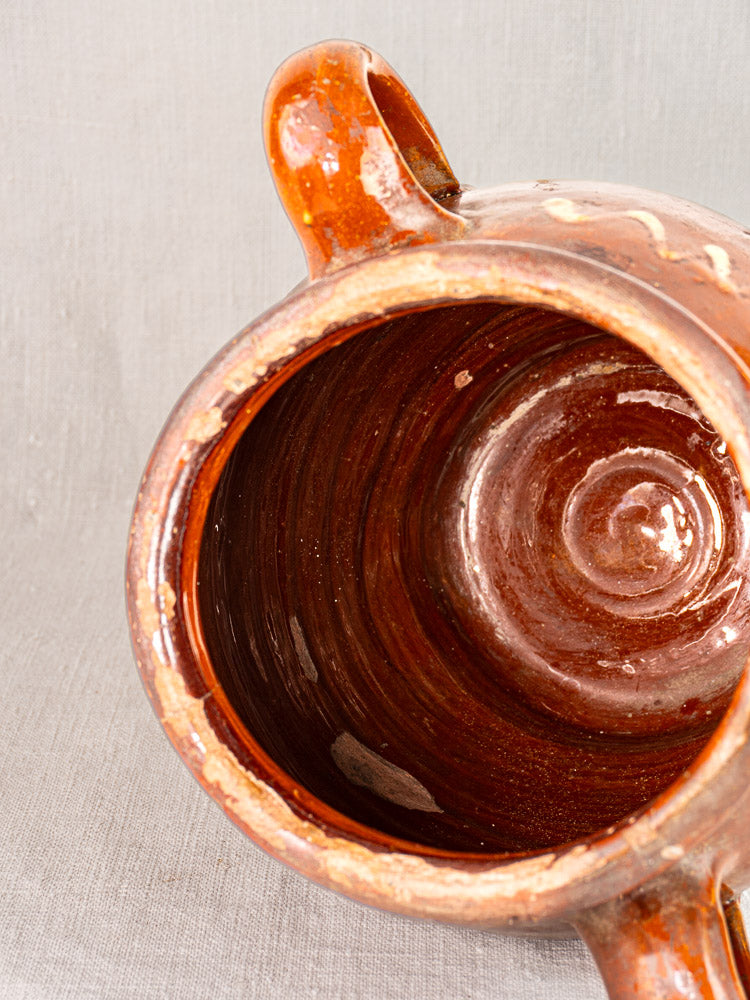 Antique French confit pot with handles, glossy brown glaze, yellow slipwork, viewed from above on a gray background.