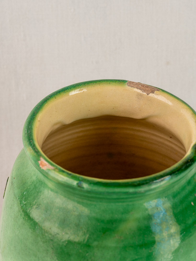 Antique French confit pot with green glazed terracotta, chipped rim, tan interior, minor edge wear, on light background.