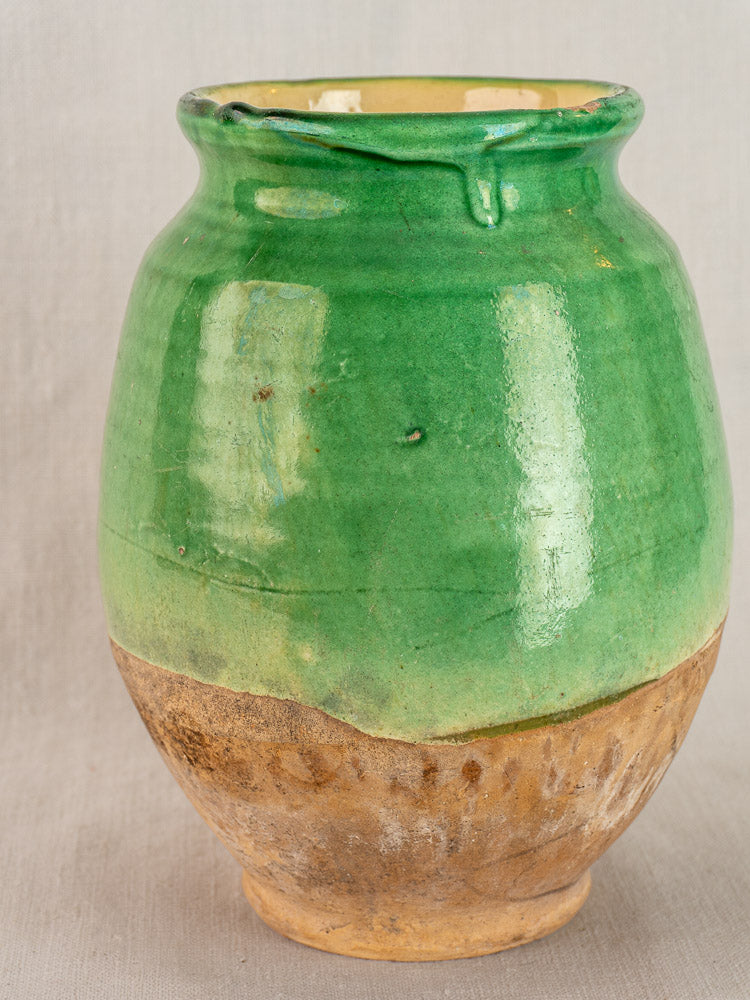 Antique French confit pot, circa 1900, with glossy green glaze and unglazed textured brown terracotta base, on neutral background.
