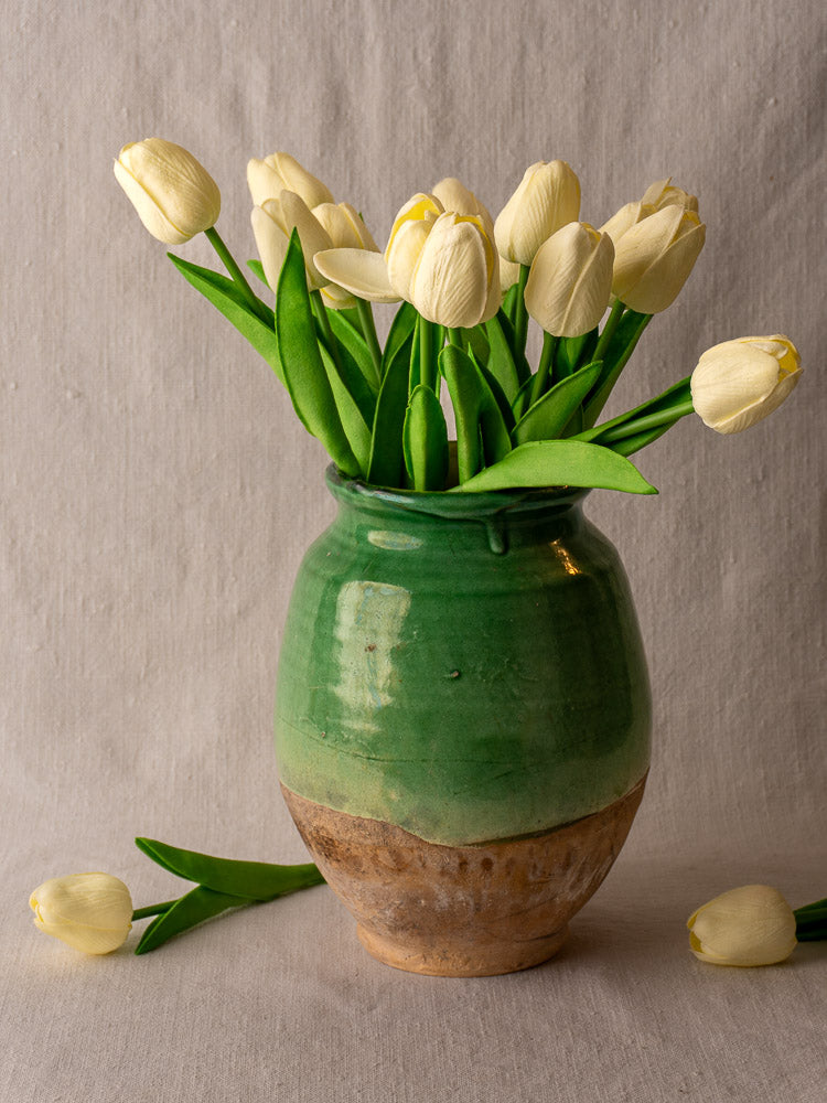 Antique French confit pot with green-glazed upper and terracotta base, set on a light gray fabric background.