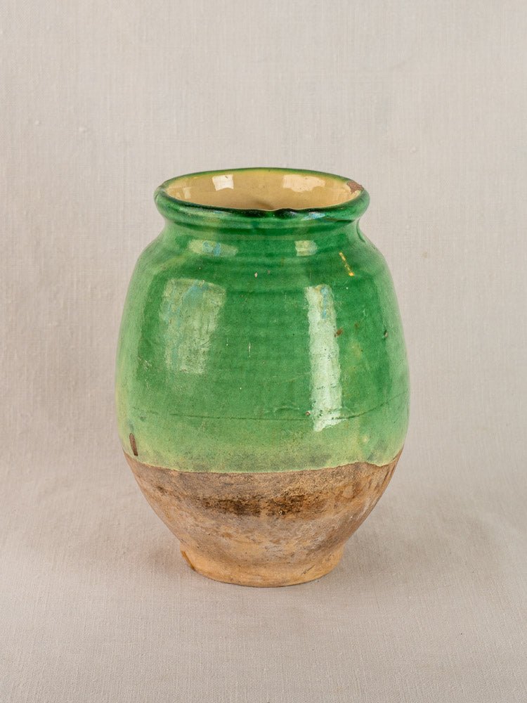 Antique French confit pot with green-glazed upper and terracotta base, set on a light gray fabric background.
