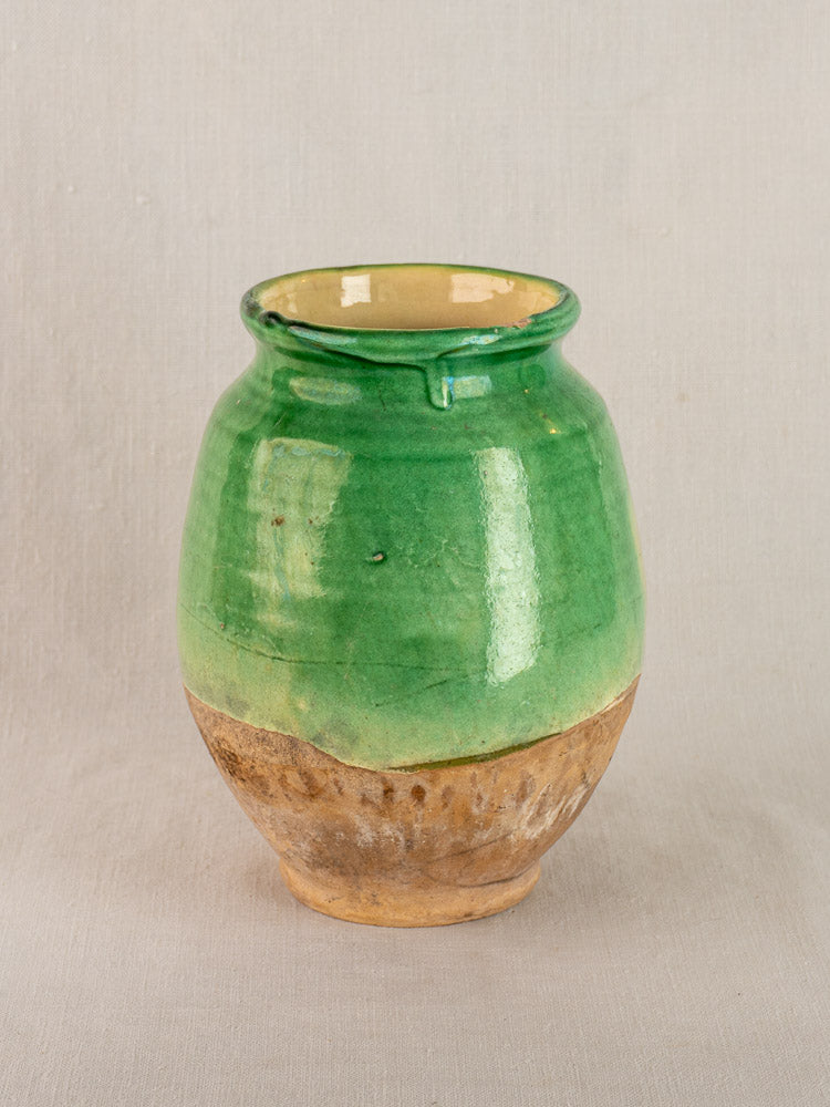 Antique French confit pot with rounded terracotta form, green glazed upper half, and unglazed brown base on light backdrop.
