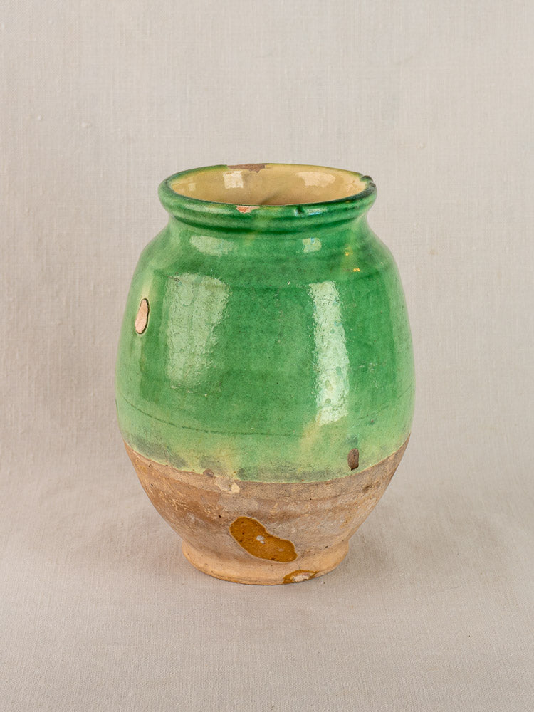 Antique French terracotta confit pot, circa 1900, with green glaze top and chipped unglazed lower half on plain light background.