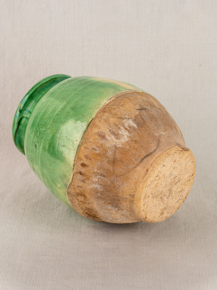 Antique French confit pot, round terracotta with green-glazed upper half, natural clay below, on plain neutral background.