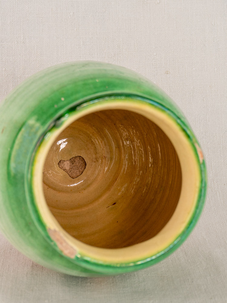 Antique French confit pot in green glazed terracotta, top view showing inner chip and minor rim wear on light textured surface.