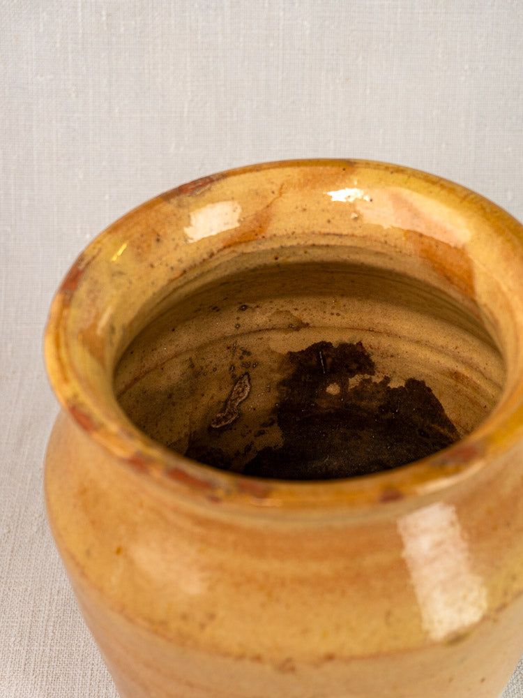Antique French confit pot, late 19th century yellow glazed terracotta with dark interior residue, on light textured surface.