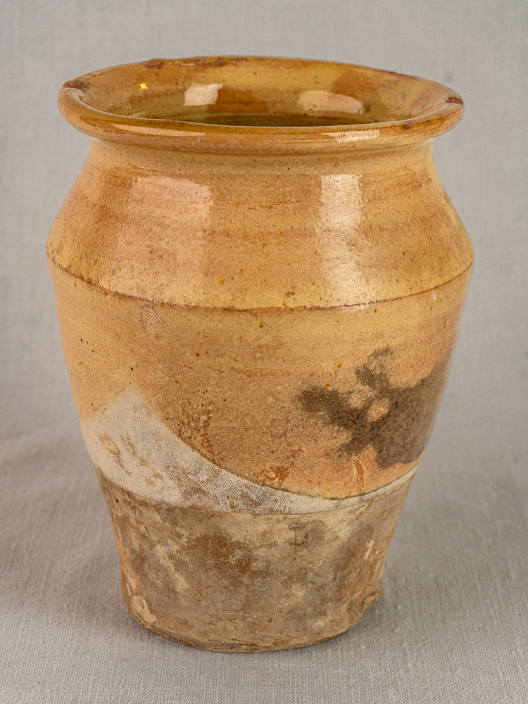 Antique French yellow glazed terracotta confit pot with wide rim and textured base on neutral fabric background.