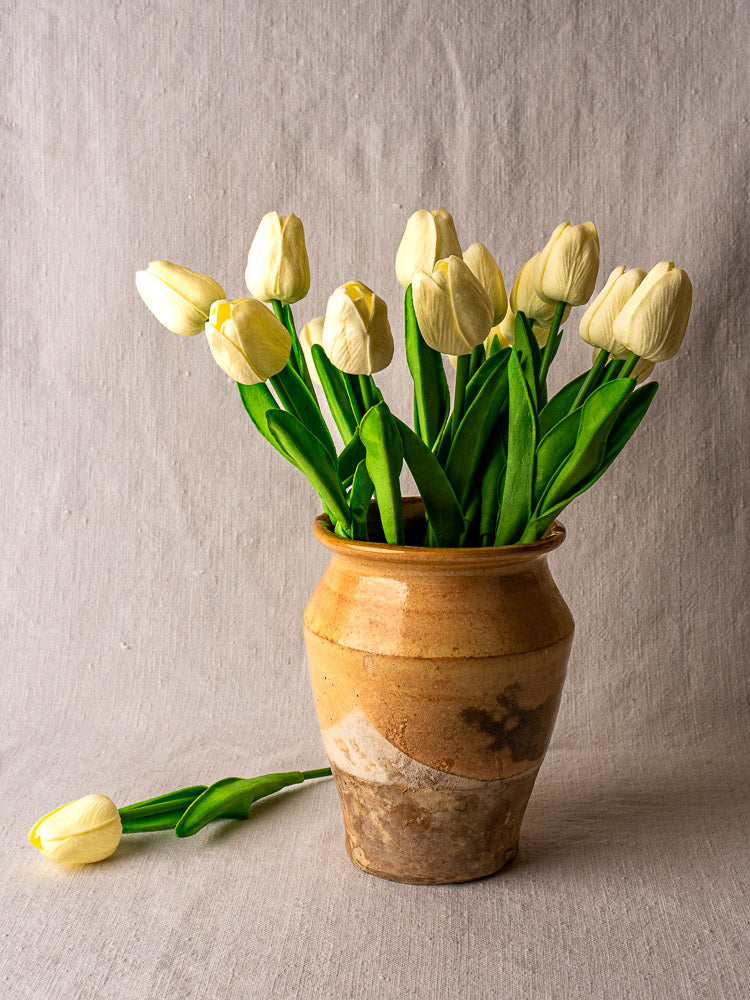 Late 19th-century French confit pot with yellow glaze holding pale tulips on beige fabric.