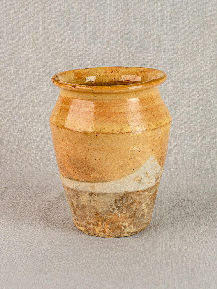 Late 19th-century French confit pot with yellow glazed terracotta, wide mouth, on neutral textured surface.