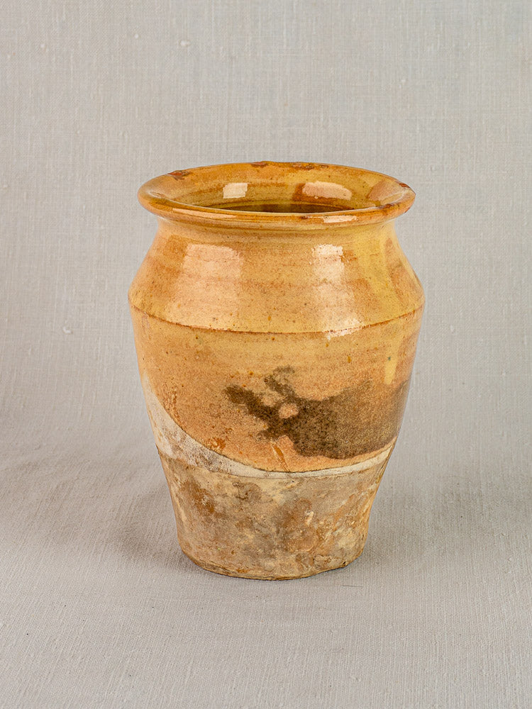 Antique French confit pot in yellow glazed terracotta with wide rim and tapered base, set on a light gray background.