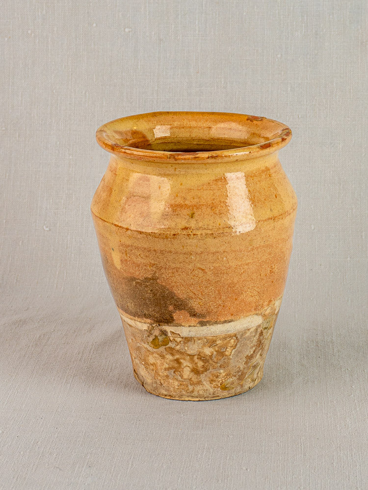 Antique French confit pot in yellow glazed terracotta with rounded rim, brown and ochre tones, set on gray background.