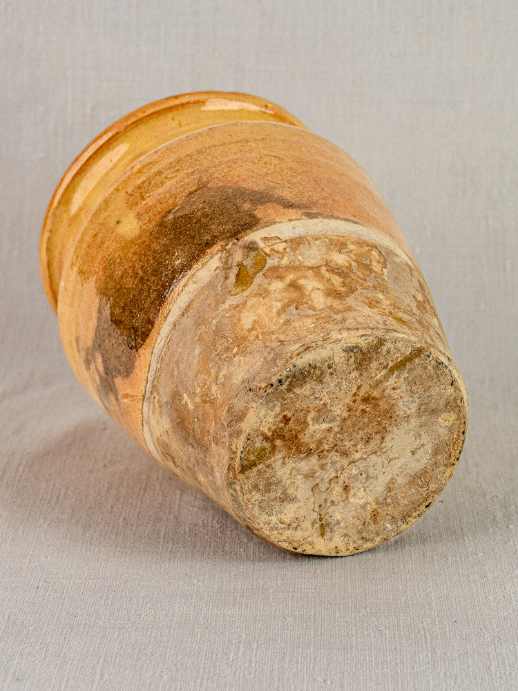 Late 19th-century French confit pot in yellow glazed terracotta with rich patina, resting on light textured surface.