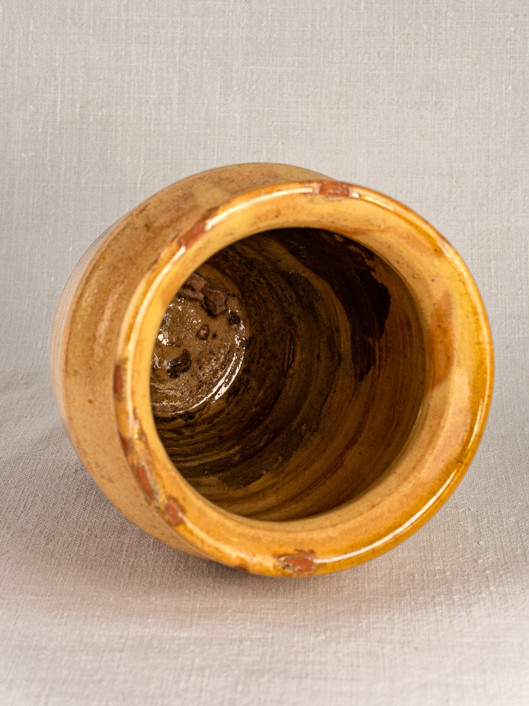 Late 19th-century French confit pot in yellow glazed terracotta with rounded rim and rustic details on a light textured surface.