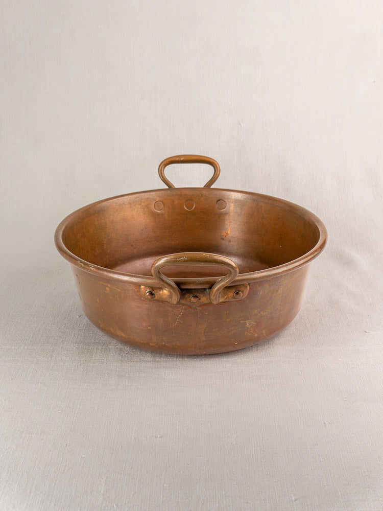Antique French copper basin with side and upright handles on a light, textured surface.