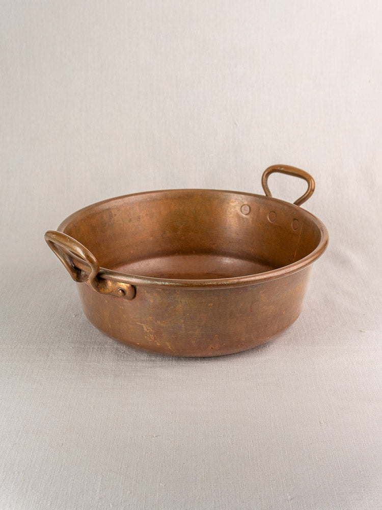 Antique French copper basins, nesting pair with large handles, shown on light beige fabric.