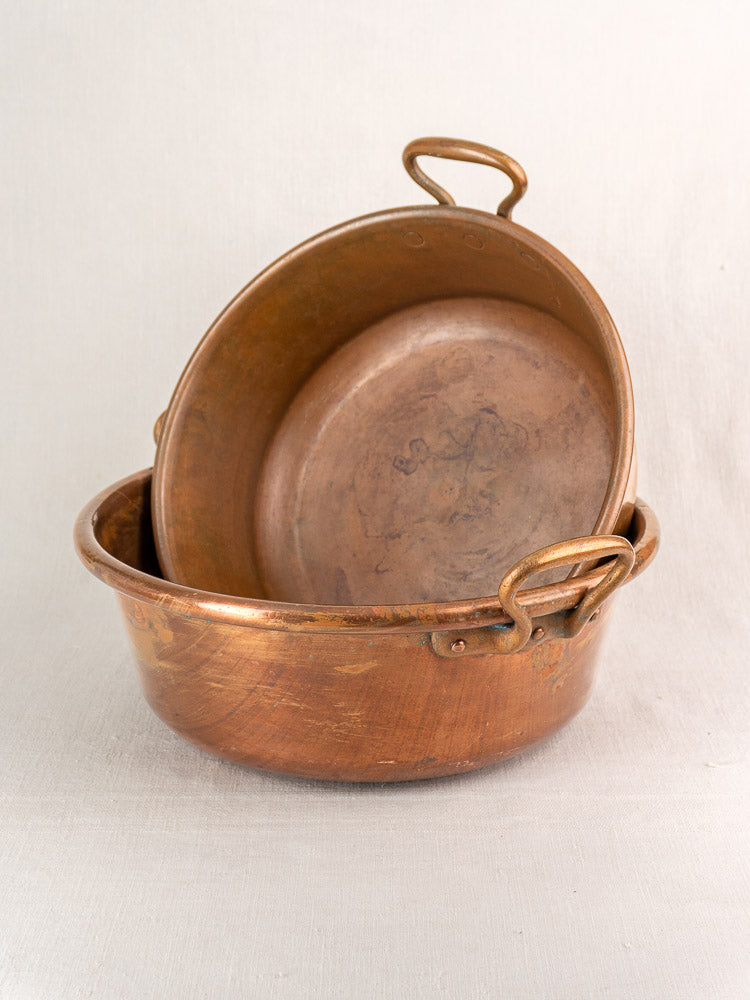 Nesting pair of late 19th c. French copper basins with handles and rustic patina on pale fabric.