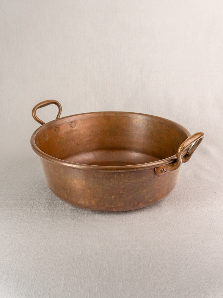 Pair of round, shallow antique French copper basins with curved handles, nesting on light fabric, late 19th century.