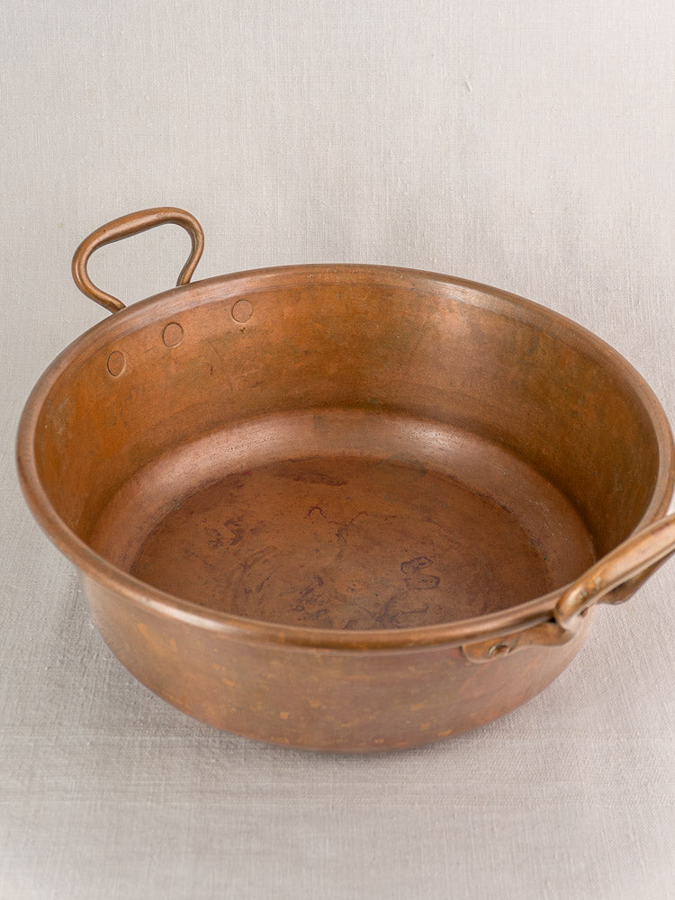Antique French copper basin with two handles and aged patina on a light textured surface.
