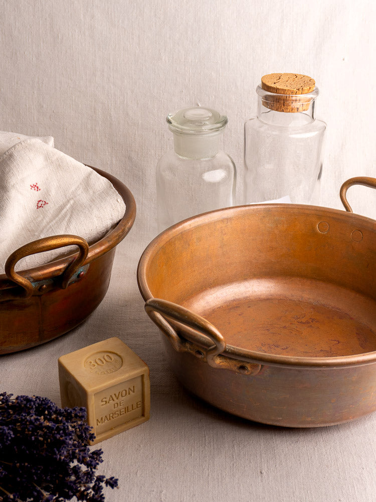 Pair of late 19th century French copper basins with handles, shown with glass jars, linen, Marseille soap, and dried lavender.
