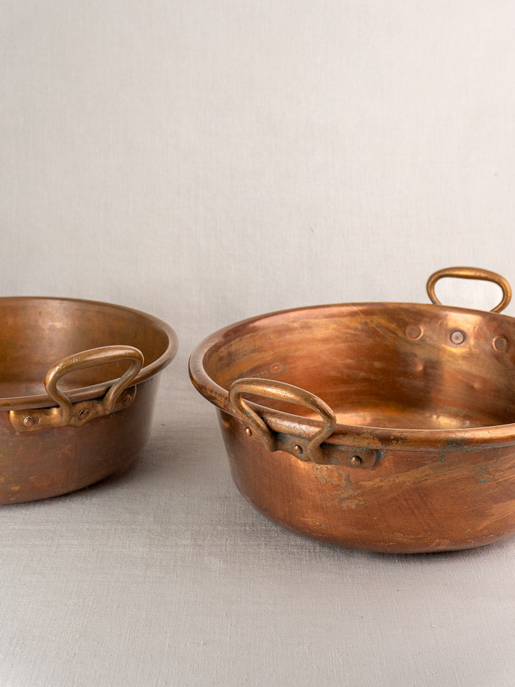 Pair of antique French copper basins with aged patina, nested on a light textured surface.