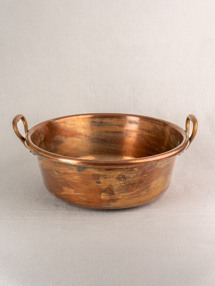 Antique French copper basin with two side handles and aged patina on a light gray surface.