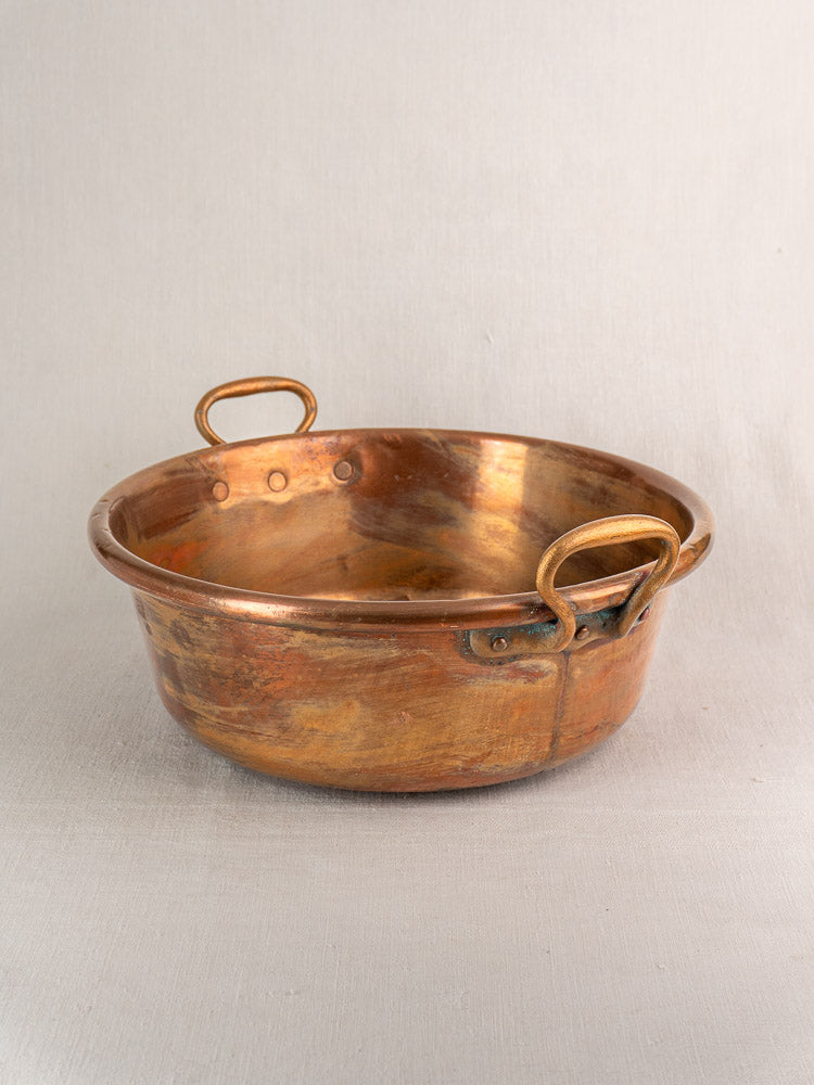Antique French copper basin with round, shallow form and two handles on a neutral surface.