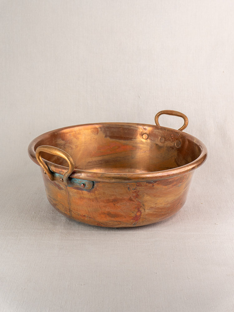 Pair of late 19th-century French copper basins with brass handles, tarnished patina, on a textured surface.