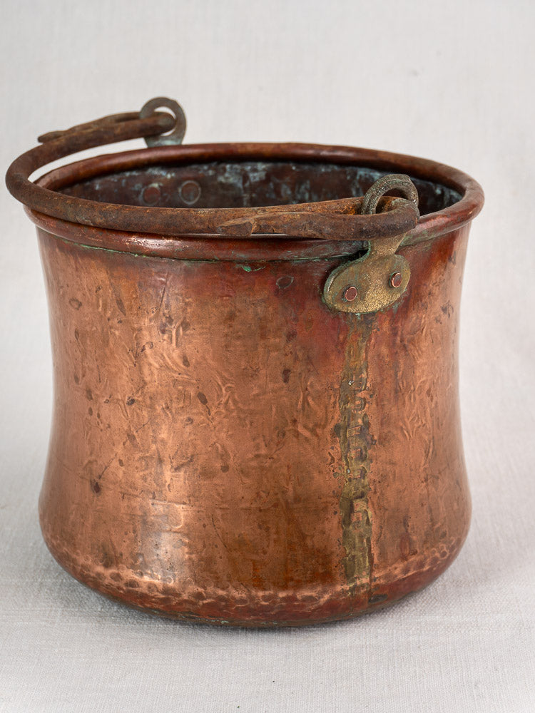 Antique French hammered copper bucket with iron swing handle, rivets, seam, and rich patina spots.
