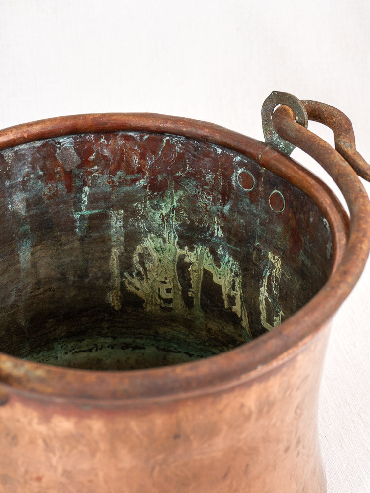 Antique French hammered copper bucket with weathered surface, greenish patina, and wrought iron handle.