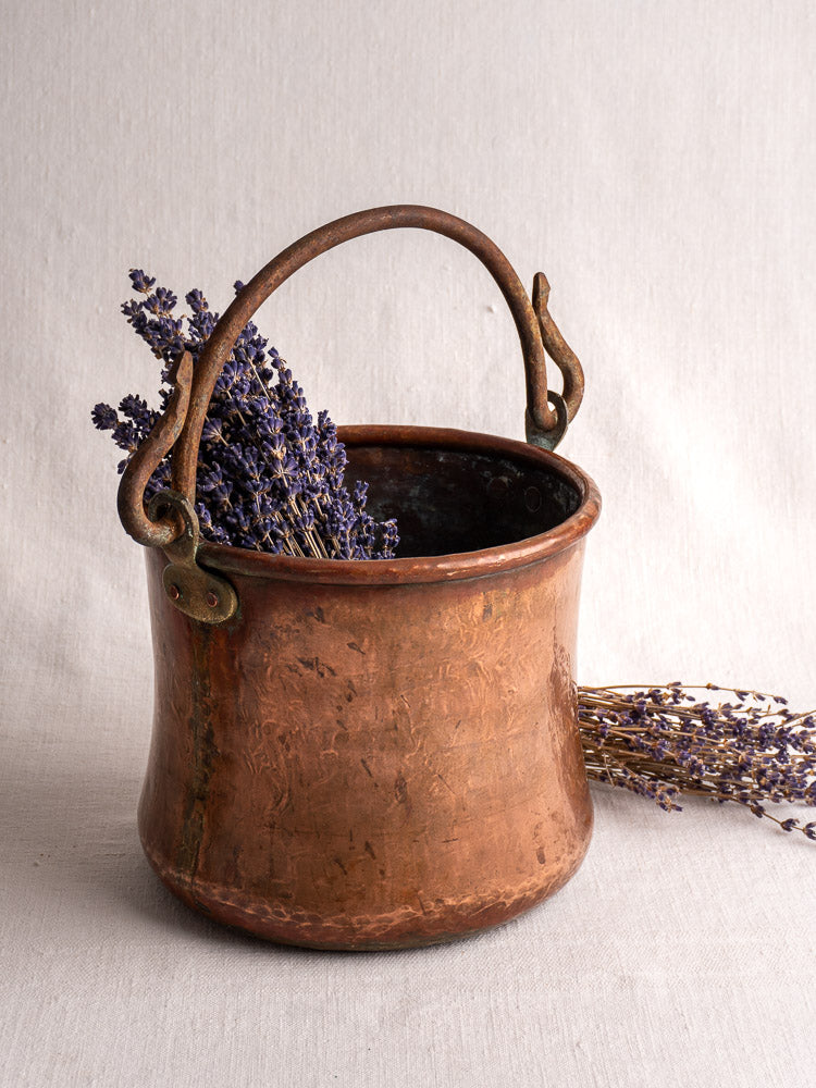 Antique French hammered copper bucket with wrought iron handle filled with dried lavender on fabric.