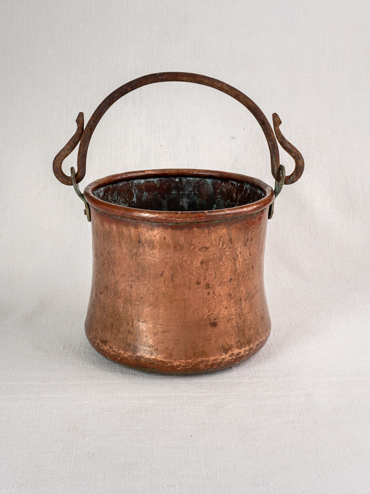 Antique French hammered copper bucket with wide opening and iron swing handle on a neutral backdrop.