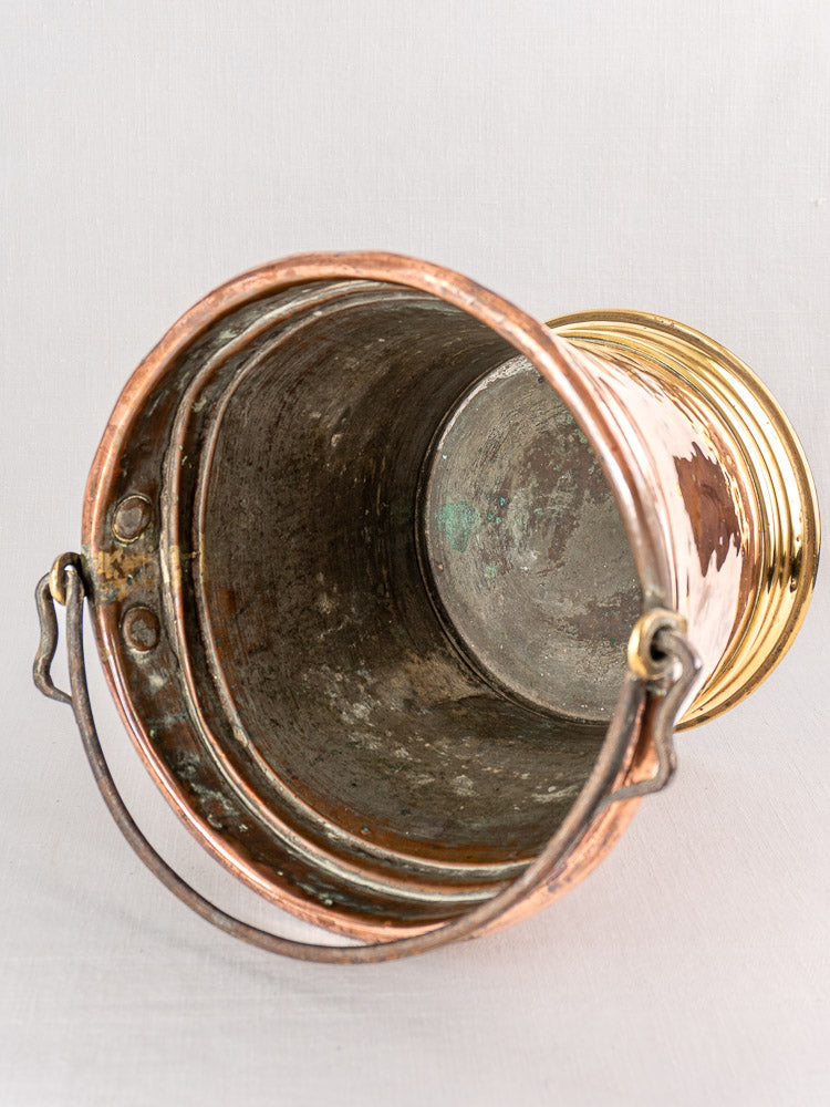 Late 19th-century French copper champagne bucket with brass base and curved handle, top view on light grey background.