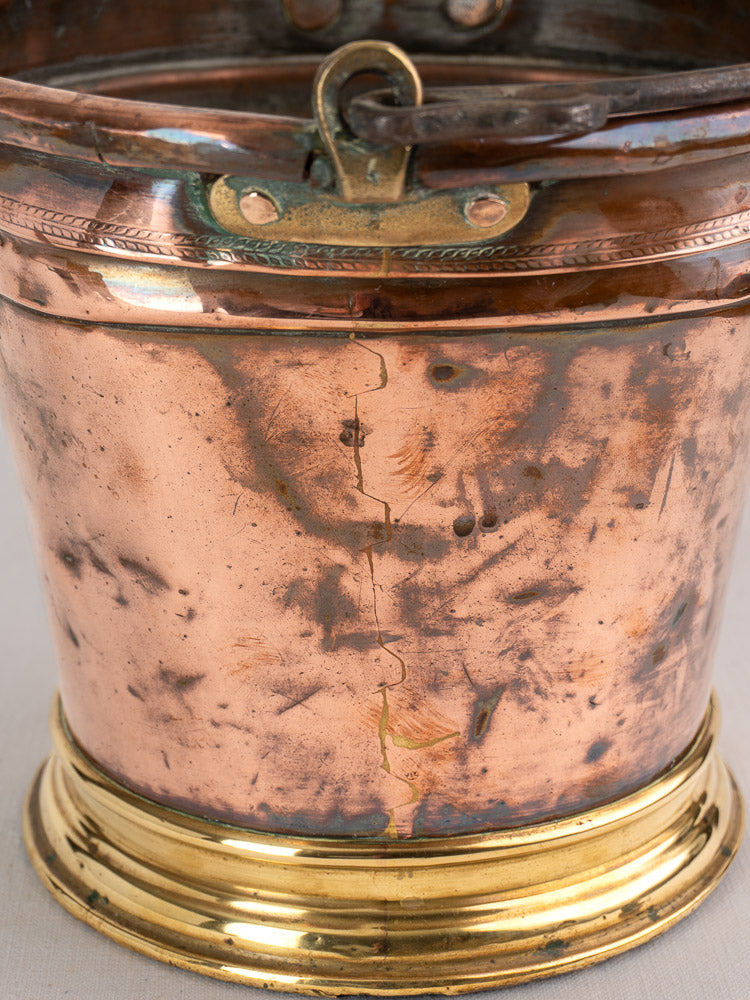 Antique French copper bucket with brass-colored base, handle attachment, vertical seam, dents, and scratches.