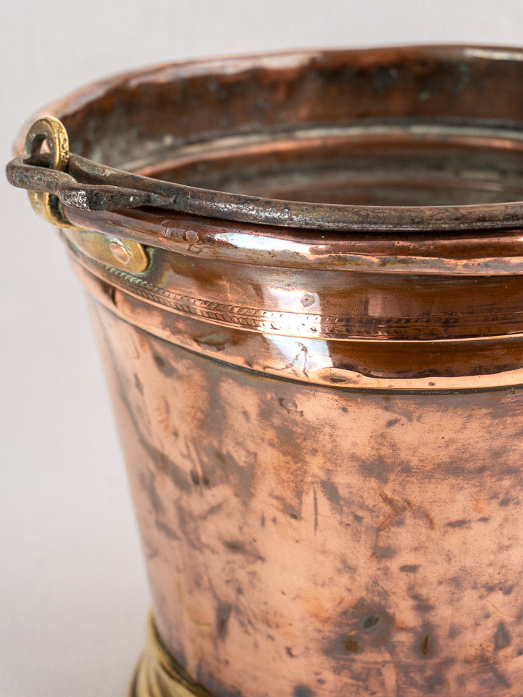 Antique French copper champagne bucket with dark metal handle, brass base, and a rich patina.