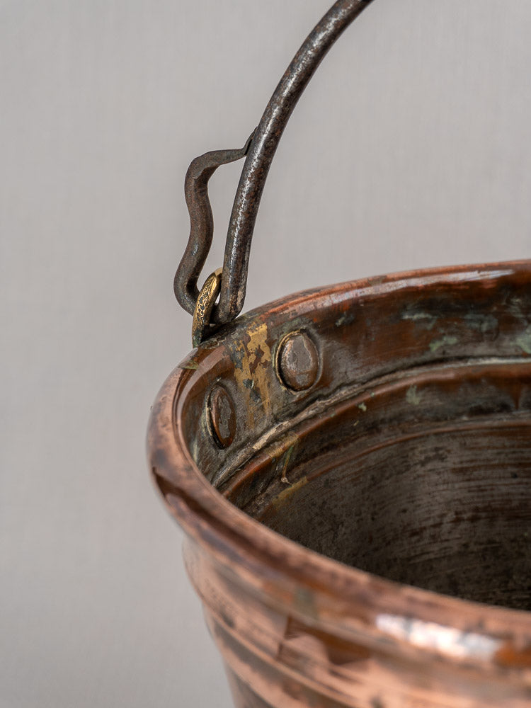 Antique French copper champagne bucket handle and rim with aged patina, rivets, set against a light background.