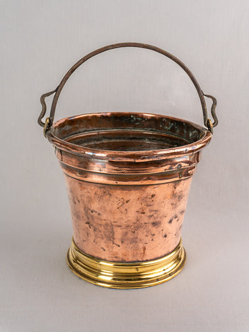 Antique French copper bucket with brass base, metal handle, and rustic patina on light gray background.