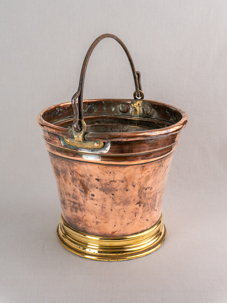 Antique French copper champagne bucket with brass base and curved handle, lightly weathered on a light gray background.