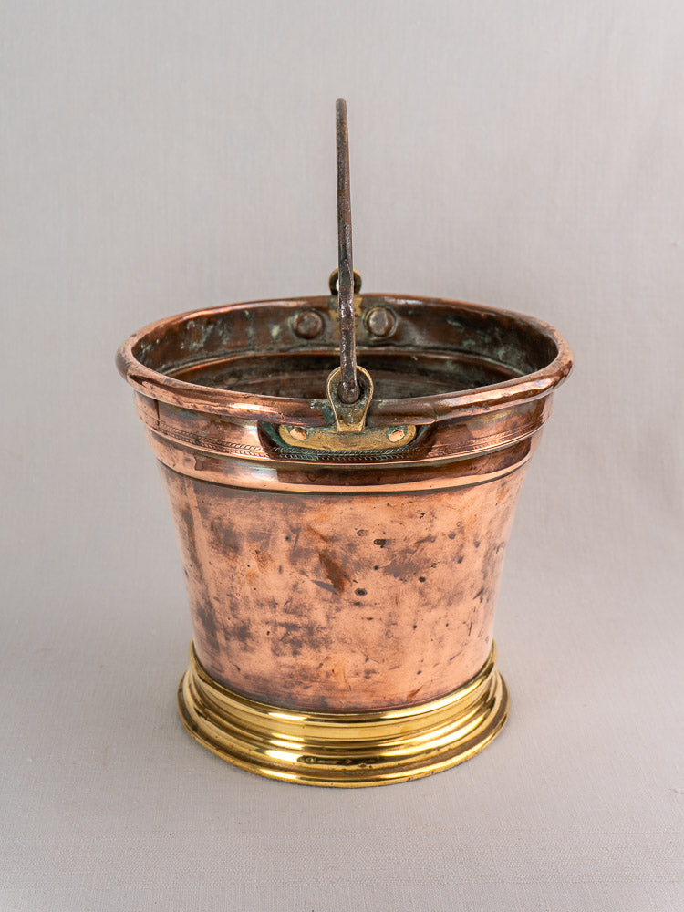 Antique French copper champagne bucket with brass base and metal handle, showing patina against a light gray background.