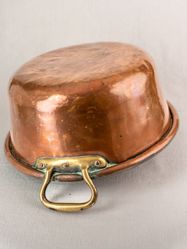 Antique French copper jam pan with brass handles, displayed upside down on neutral fabric.