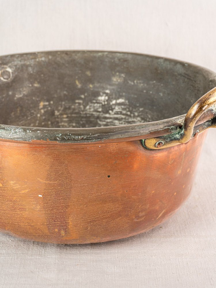 Antique French copper jam pan with brass handles, late 19th century, on pale fabric surface.