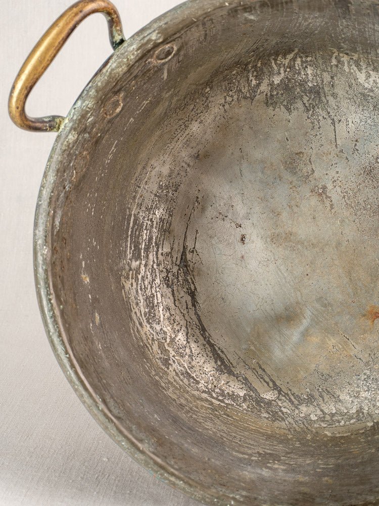 Antique French copper jam pan with brass handles, tarnished interior, on light fabric surface.