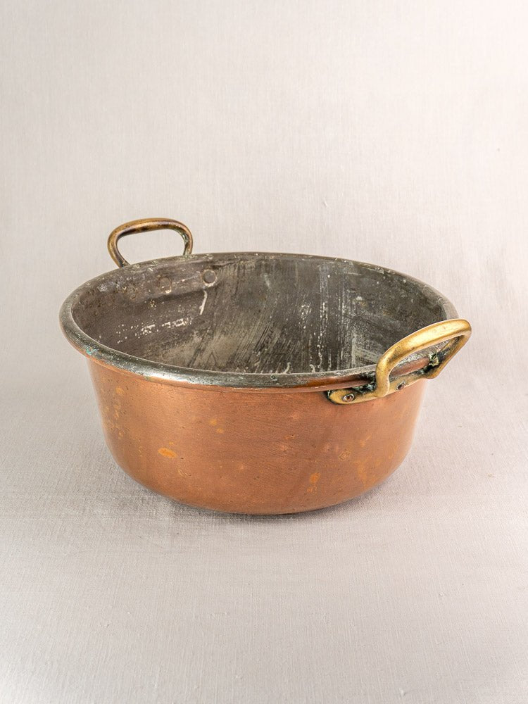 Large antique French copper jam pan with brass handles, gently worn and resting on a neutral surface.