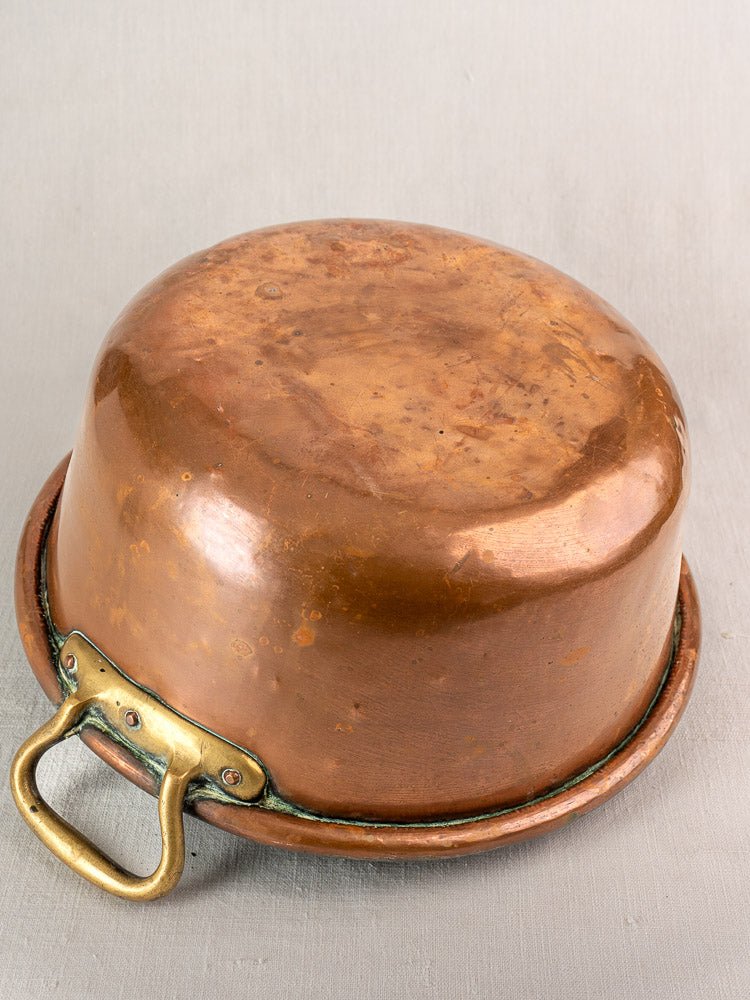 Antique French copper jam pan with brass handles, shown upside down on neutral fabric to display patina.