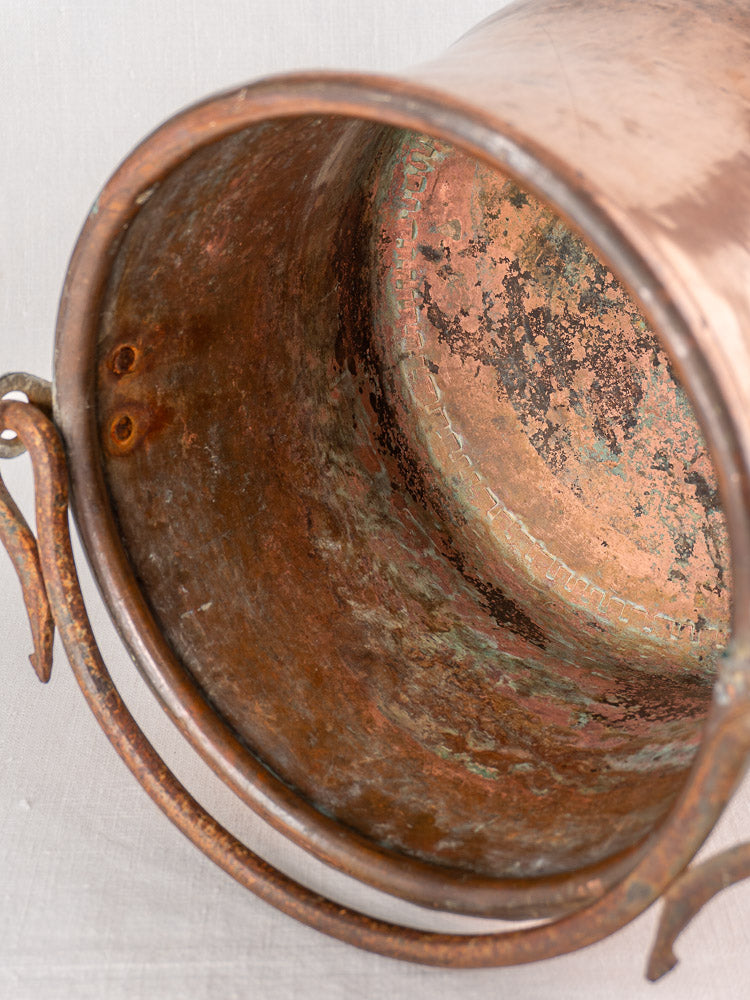 Antique French hammered copper cauldron with iron bail handle, featuring weathered patina and coppersmith oxidation details.