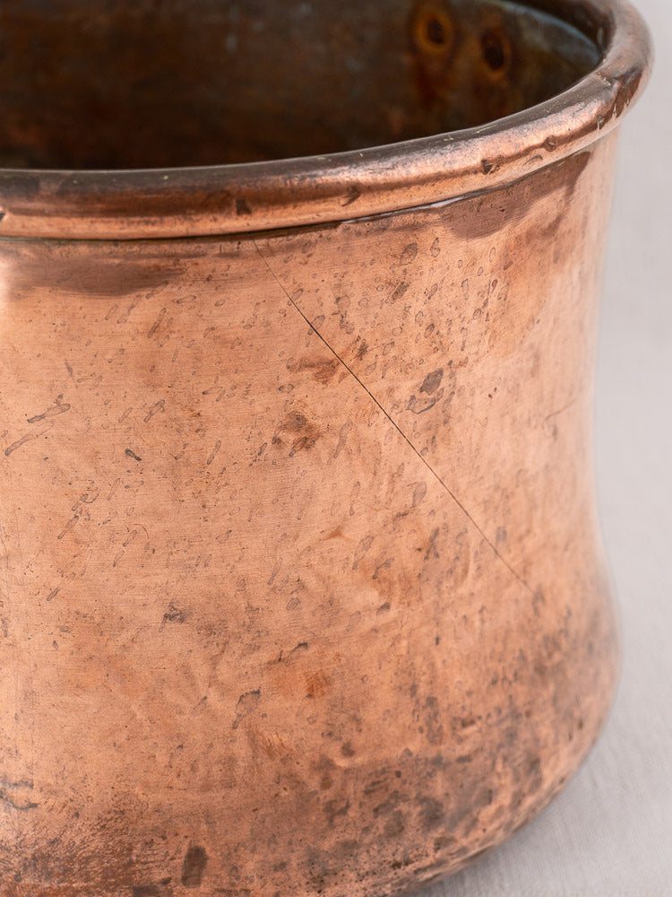 Antique French copper cauldron with hand-hammered texture, iron handle, flared rim, and rich patina on light background.