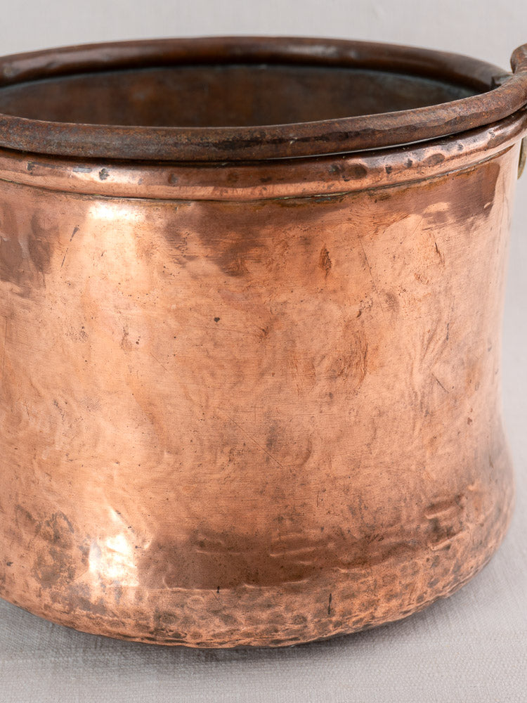 Antique French copper cauldron with hammered body, iron bail handle, flared base, and aged textured surface.