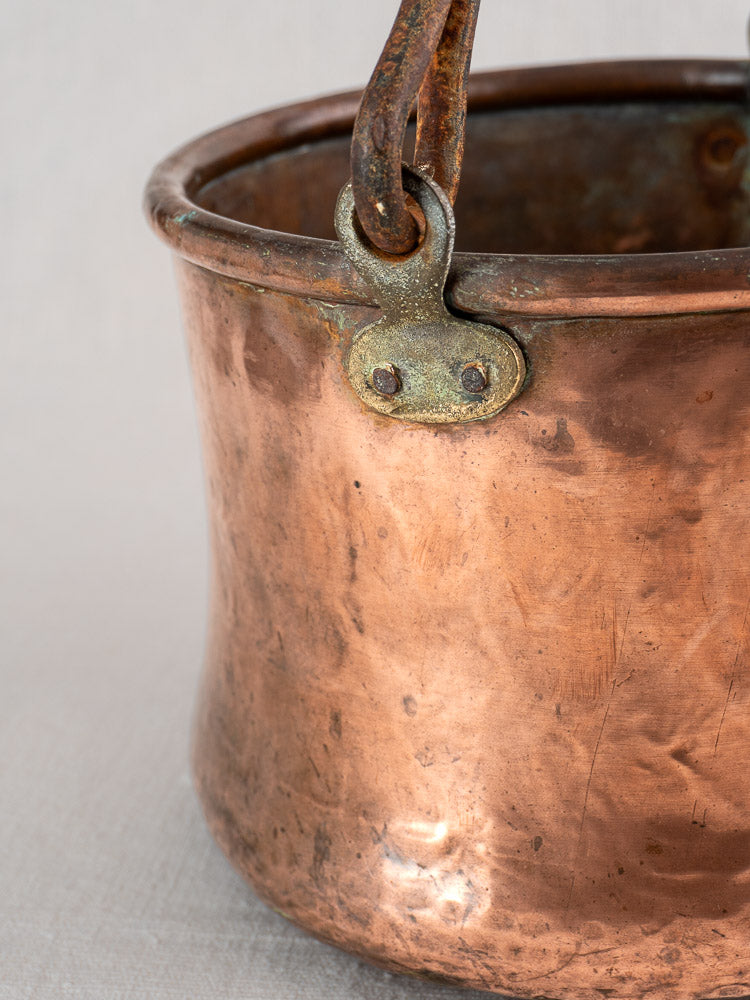 Antique French hammered copper cauldron with riveted iron bail handle, coppersmith marks; plain neutral background.