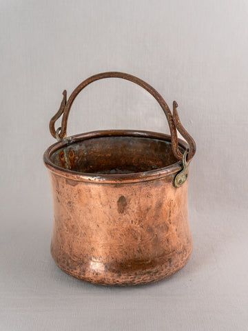 Antique French copper cauldron, hand hammered with iron bail handle and aged patina on light gray background.